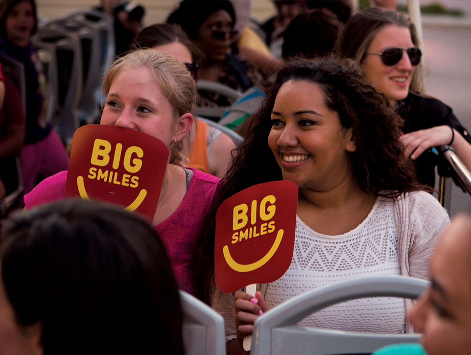 Two ladies onboard a Big Bus holding branded signs